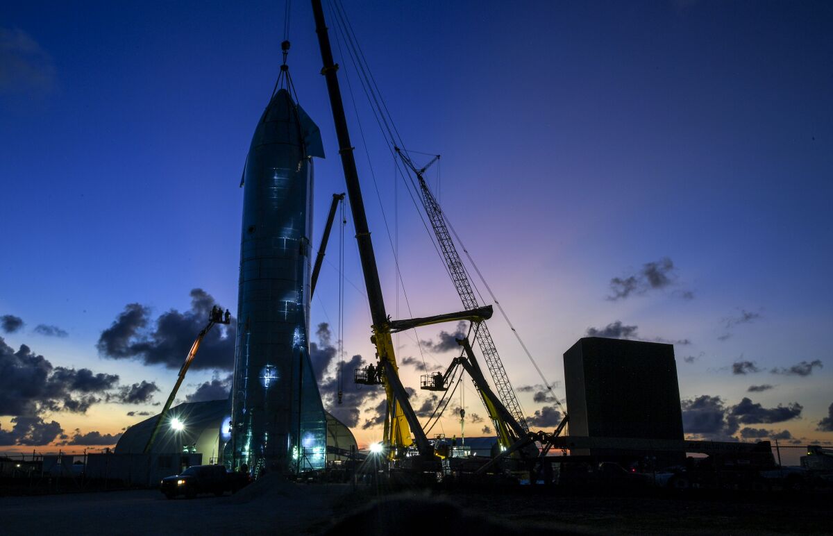A crane operates near the top of a SpaceX Starship test rocket.