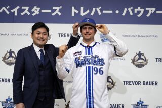 Trevor Bauer porta el uniforme y gorra del Yokohama DeNA BayStars junto al director de operaciones del equipo Tatsuhiro Hagiwara en la conferencia de prensa de su presentación con el equipo el viernes 24 de marzo del 2023. (AP Foto/Eugene Hoshiko)