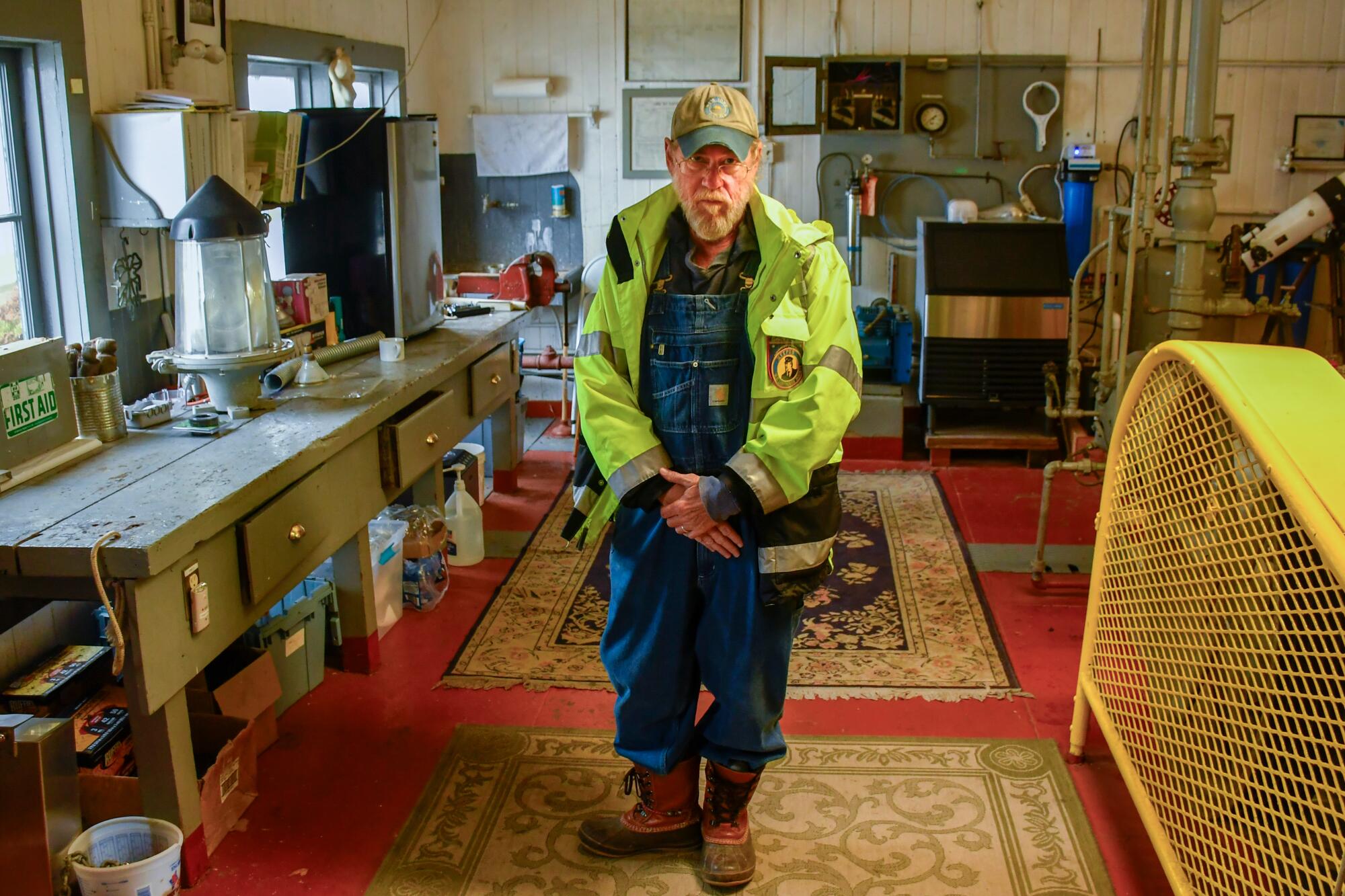 A man in denim overalls and a yellow windbreaker in a room at a lighthouse 