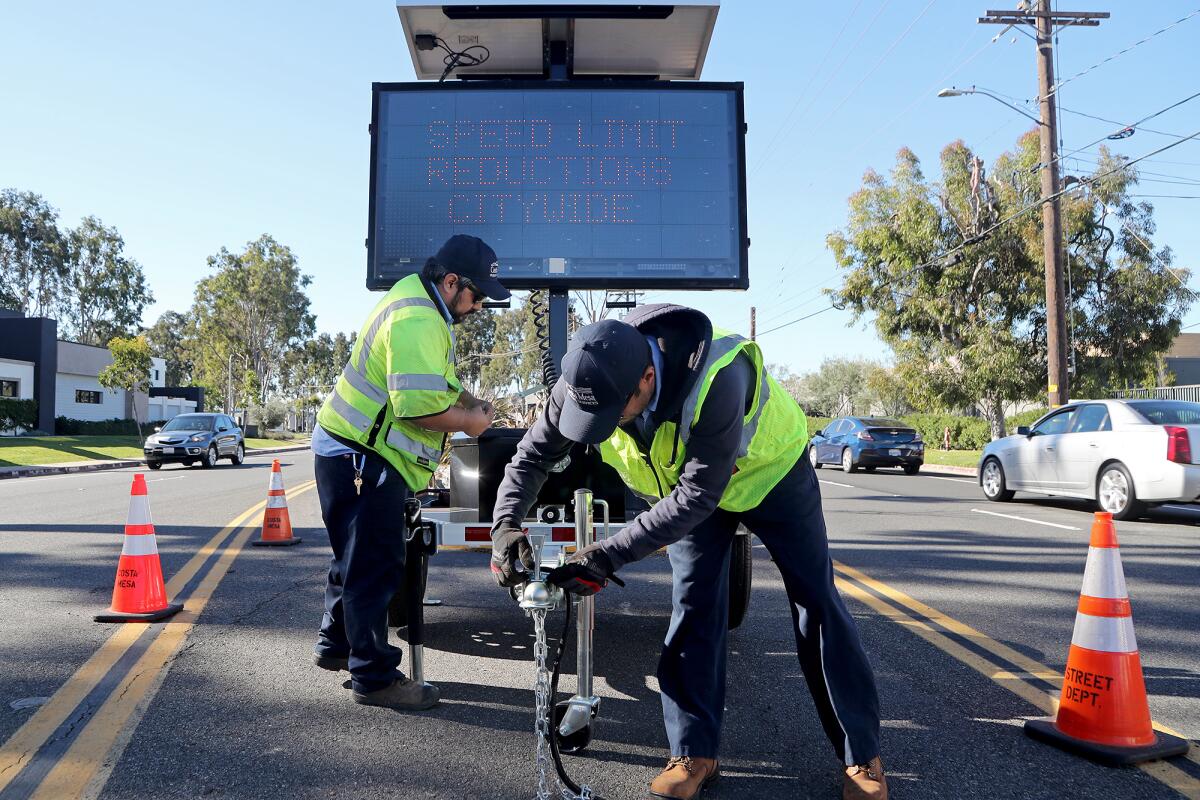 Maintenance workers Henry Granados, left, and Daniel Solis set up a sign along Red Hill Avenue in Costa Mesa Tuesday.