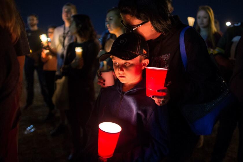 LAS VEGAS, NV - OCTOBER 2, 2017: Keli McDade of Las Vegas leans on her son Ayden during a candle light vigil at Town Square to remember those killed and injured the day after a lone gunman open fired onto a county music festival from the 32nd floor of Mandalay Bay hotel killing 59 and wounding 527 people on October 2, 2017 in Las Vegas, Nevada. The Mandalay Bay hotel glows in the background.(Gina Ferazzi / Los Angeles Times)
