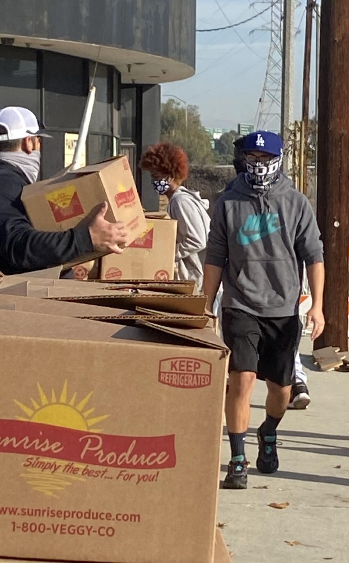 Angelou High quarterback Omar Sahagun, right, helps move 25-pound food boxes to distribute to community members.