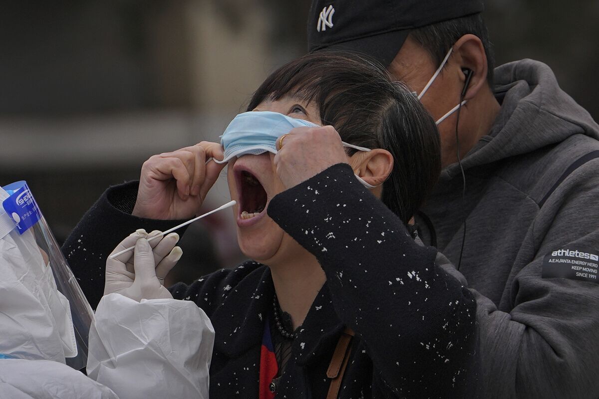 A woman pulls up her mask to get her throat swab at a coronavirus testing site near residential buildings, Wednesday, April 6, 2022, in Beijing. (AP Photo/Andy Wong)