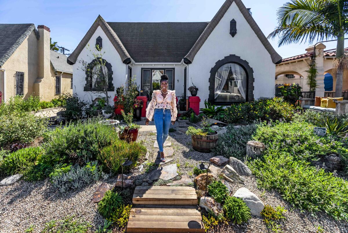 A woman walks on a path in front of a house through a landscaped yard.