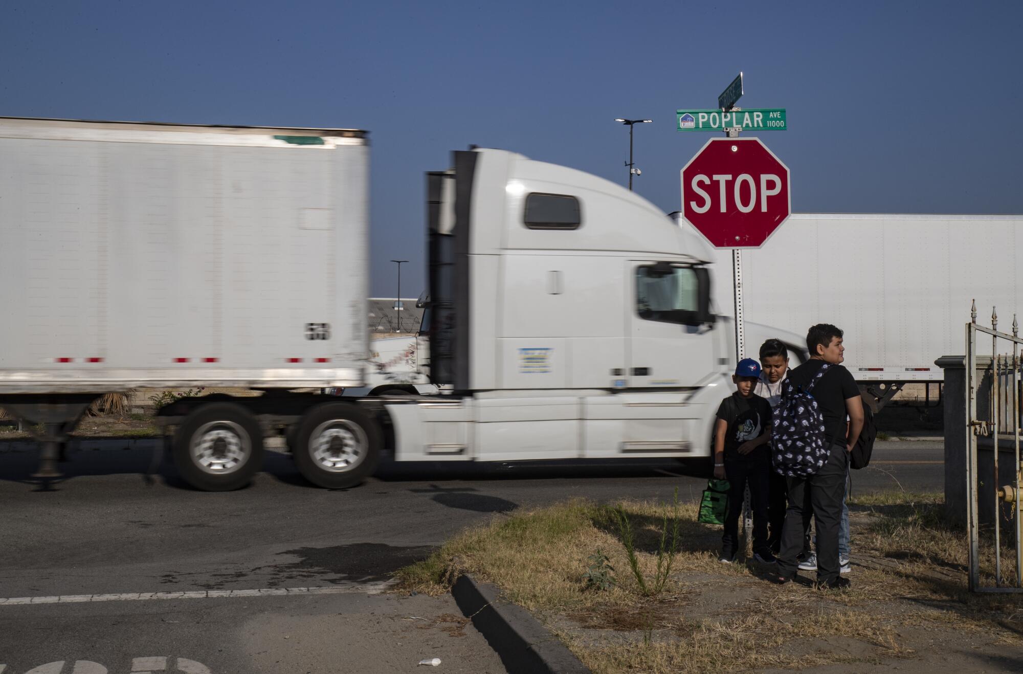 Trucks pass schoolchildren waiting at a bus stop in Fontana.