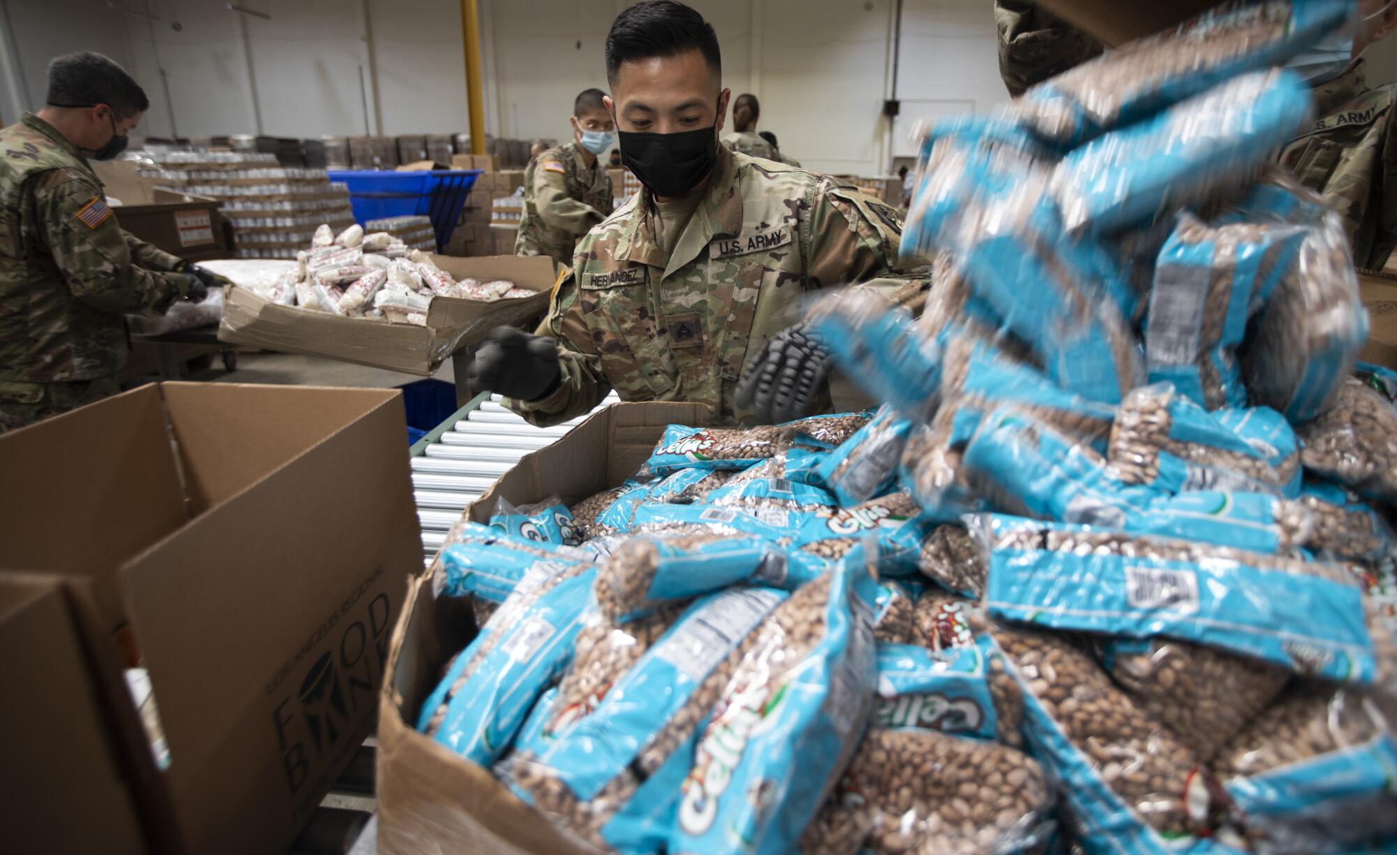 A National Guardsman stands in front of a box full of packaged nuts.