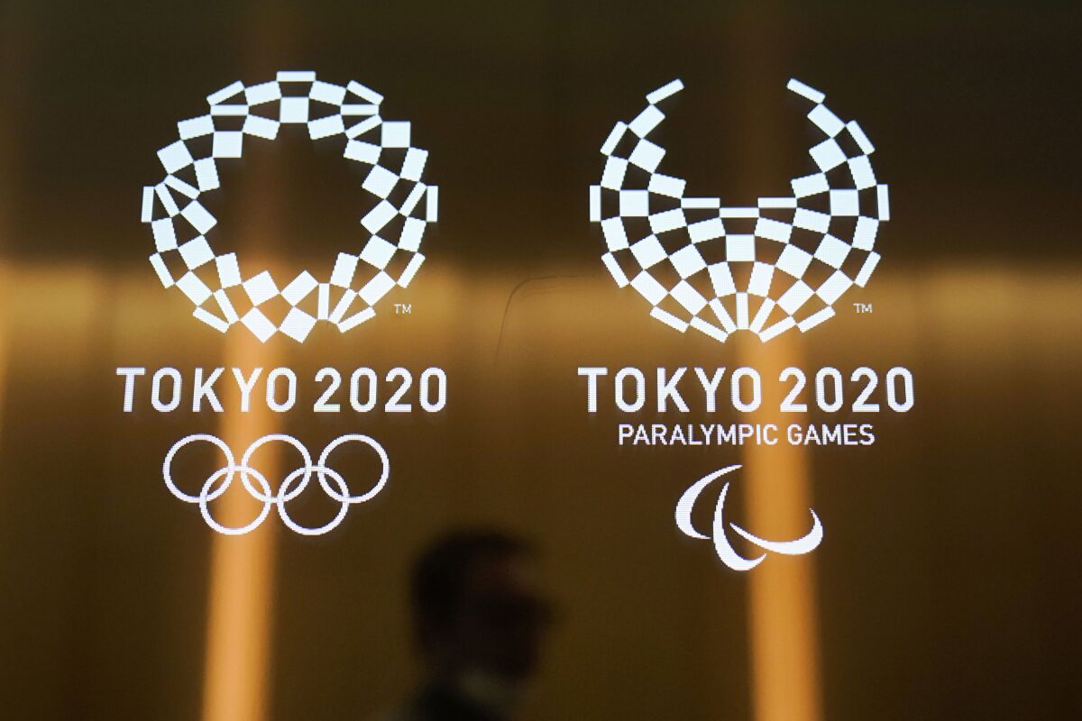  In this June 11, 2019, file photo, a man walks past the logos of the Tokyo 2020 Olympics and Paralympics in Tokyo. 