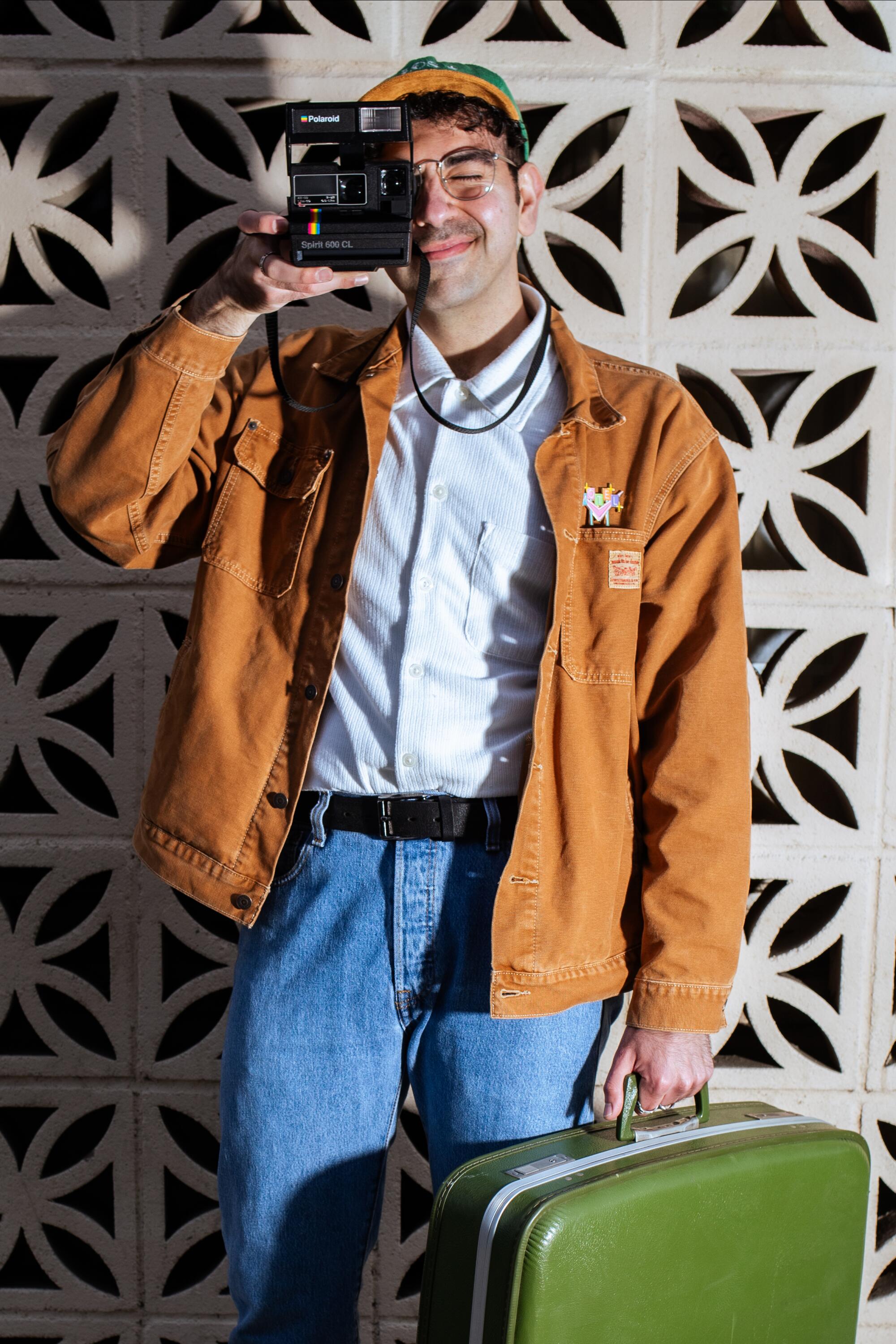 Barkev Msrlyan stands successful beforehand of a breeze artifact partition with a camera to his oculus portion holding a greenish vintage suitcase.