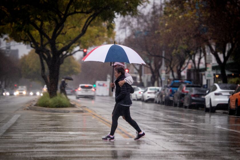 Pasadena, CA - February 24: Pedestrians toting an umbrella walk across the street amidst heavy rain in Pasadena on Friday, Feb. 24, 2023 in North Hollywood,. Southern California has only gotten a taste of the powerful winter storm system that forecasters say will bring an extended period of cold temperatures, high winds and snow, prompting the region's first blizzard warning on record.(Allen J. Schaben / Los Angeles Times)