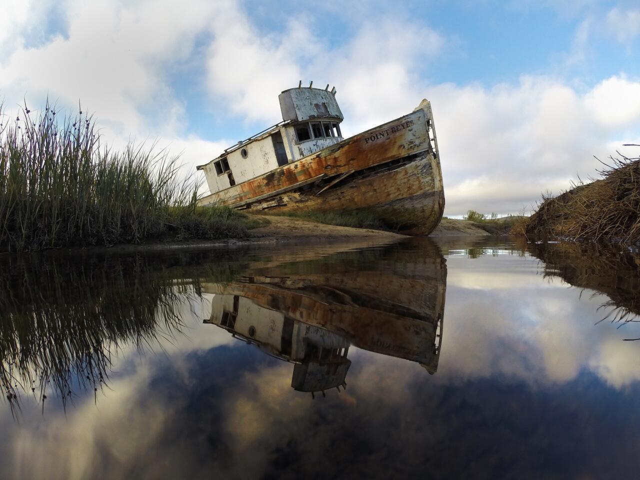A marooned fishing boat is reflected in low tide pools along Tomales Bay at Point Reyes National Seashore.