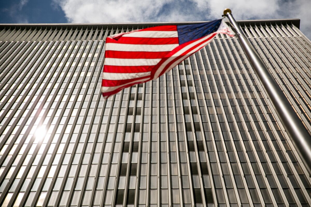 A view from below of a sunlit high-rise office building's facade with an American flag flying in front of it