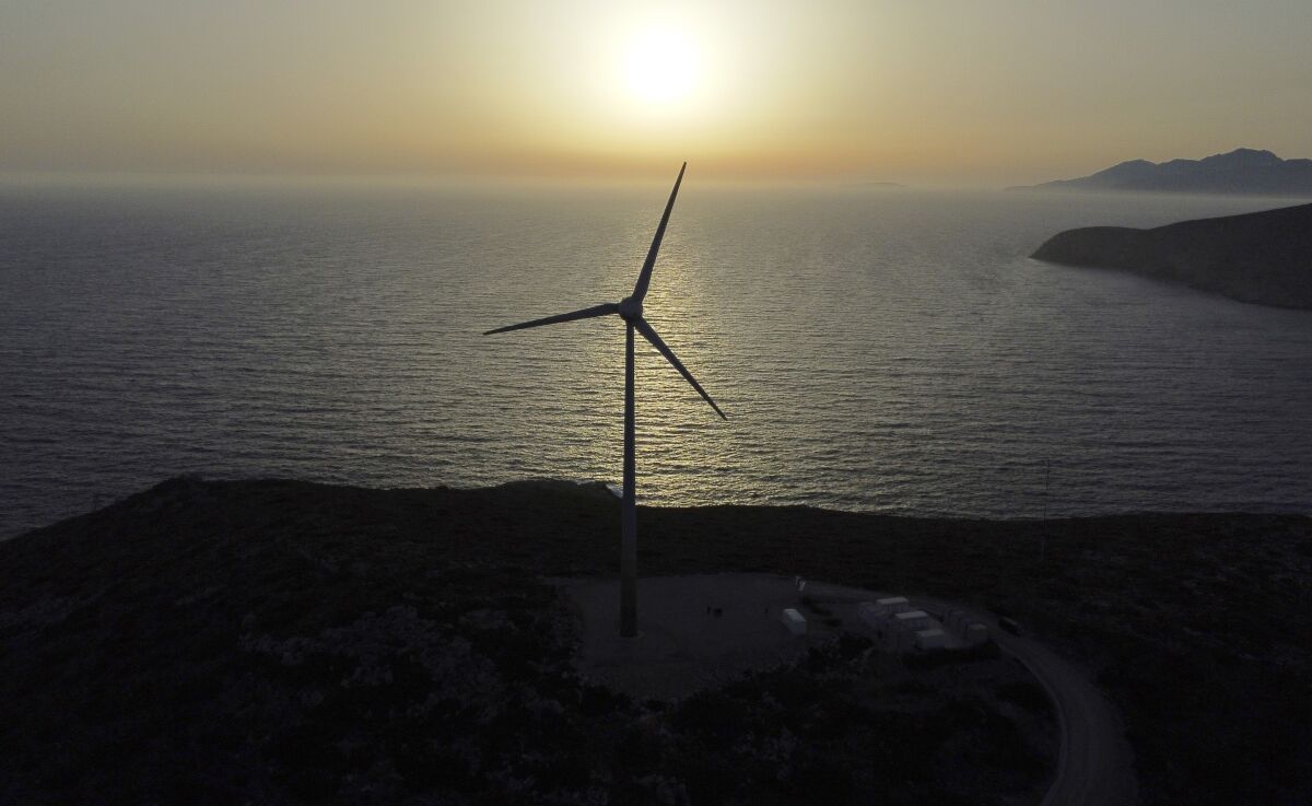 The sun sets behind a wind turbine on the Aegean Sea island of Tilos, southeastern Greece, Monday, May 9, 2022. When deciding where to test green tech, Greek policymakers picked the remotest point on the map, tiny Tilos. Providing electricity and basic services, and even access by ferry is all a challenge for this island of just 500 year-round inhabitants. It's latest mission: Dealing with plastic. (AP Photo/Thanassis Stavrakis)