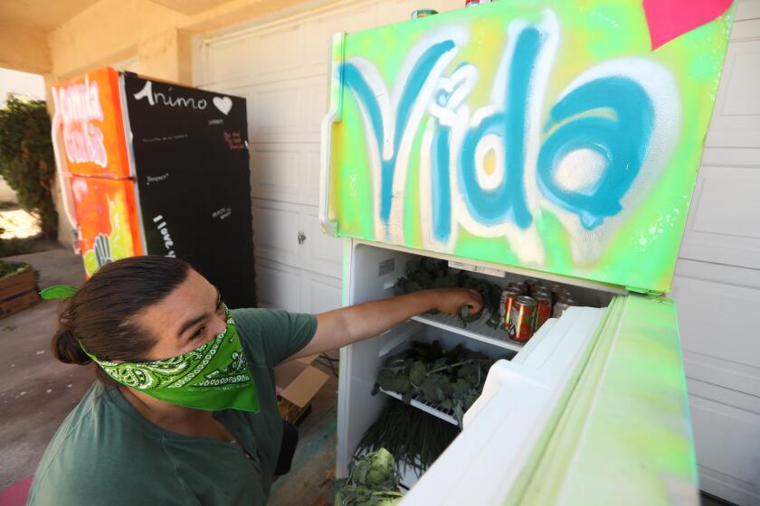 LOS ANGELES, CA - JULY 12, 2020 - - Paloma Vergara loads up a community refrigerator with items donated by Emilia Shaffer-Del Valle to the Reach 4 The Top L.A. Mid City Fridge in Los Angeles on July 12, 2020. Vergara works with Reach 4 The Top which provides transitional housing at 5044 West 21st Street. The community refrigerator is available 24 hours a day at the location. Community fridges are popping up all over Los Angeles as part of a mutual aid project to feed people in need during the coronavirus pandemic. The fridges are painted with murals and bright colors, and are stocked with food inside donated by people from the community, local food banks and restaurants. (Genaro Molina / Los Angeles Times)