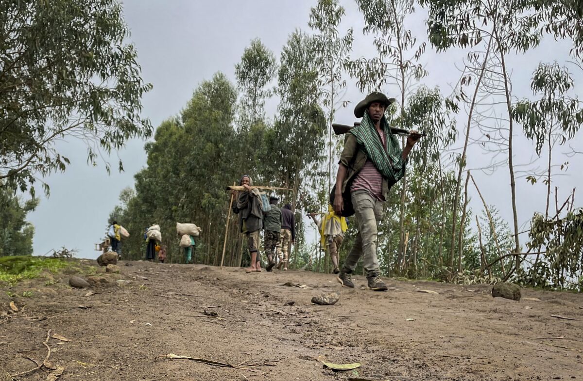 An unidentified armed militia fighter walks down a path as villagers flee with their belongings in the other direction, near the village of Chenna Teklehaymanot, in the Amhara region of northern Ethiopia Thursday, Sept. 9, 2021. At the scene of one of the deadliest battles of Ethiopia's 10-month Tigray conflict, witness accounts reflected the blurring line between combatant and civilian after the federal government urged all capable citizens to stop Tigray forces "once and for all." (AP Photo)
