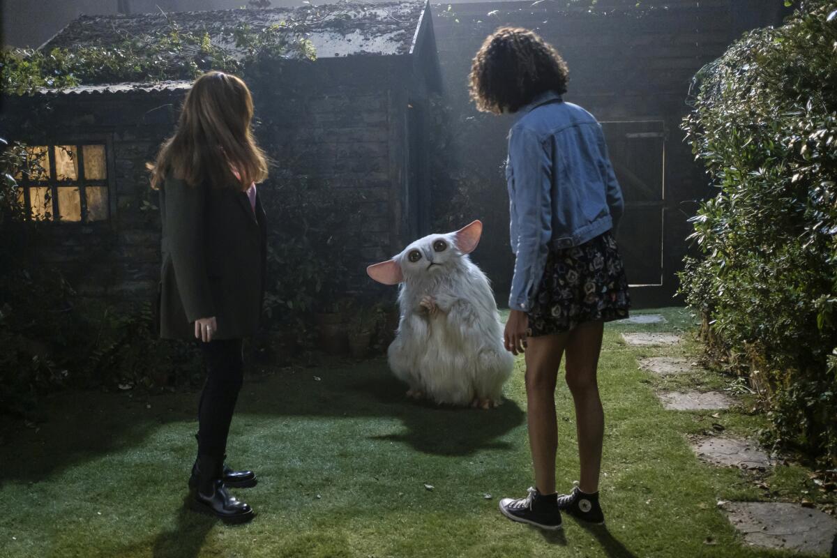 Donna Noble and Rose look at a white furry alien who is standing in a yard with a shack in the background.
