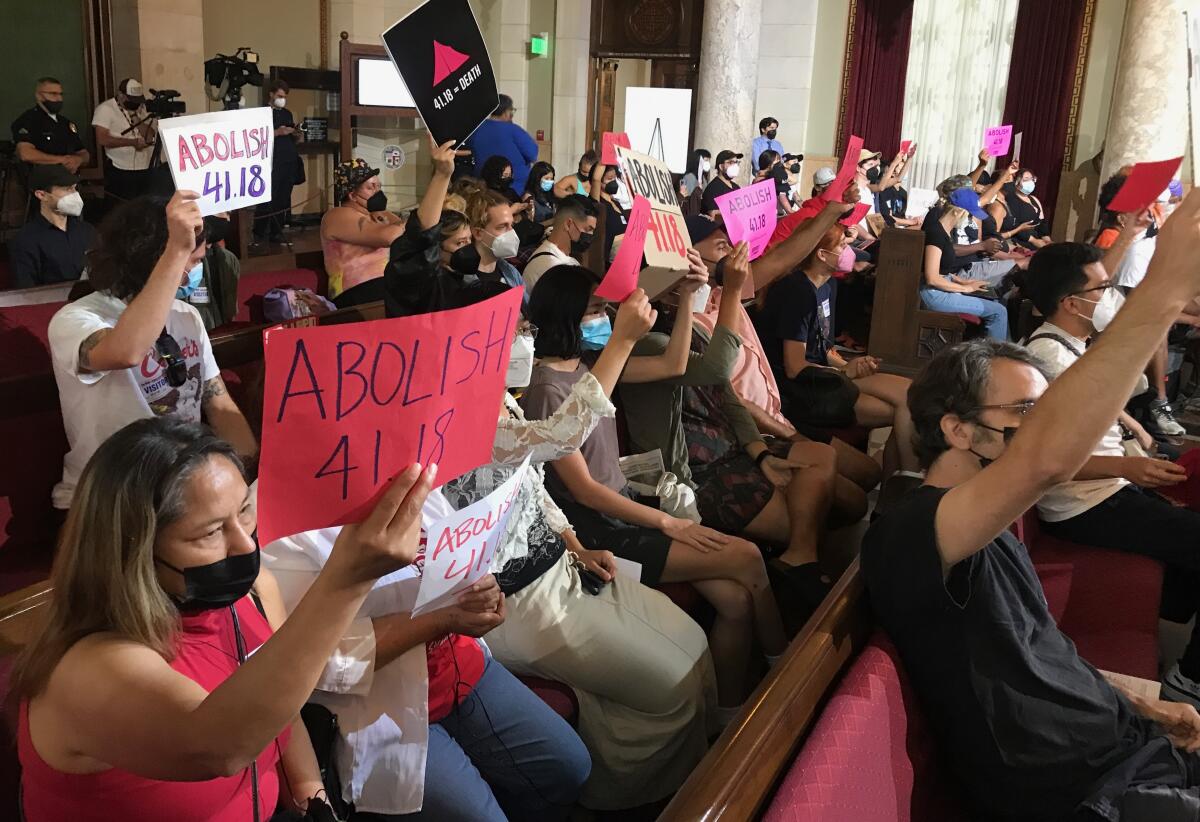 LOS ANGELES CA AUGUST 9, 2022 - Members of Services Not Sweeps, a local housing coalition, hold signs inside City Hall during council meeting, where a vote on expanding the 41.18 ordinance -- banning homeless encampments within 500 feet of schools and daycare centers is expected. (Genaro Molina/Los Angeles Times)