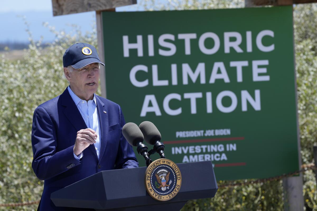 President Biden speaking outdoors in front of a large green sign reading "Historic climate action / Investing in America"