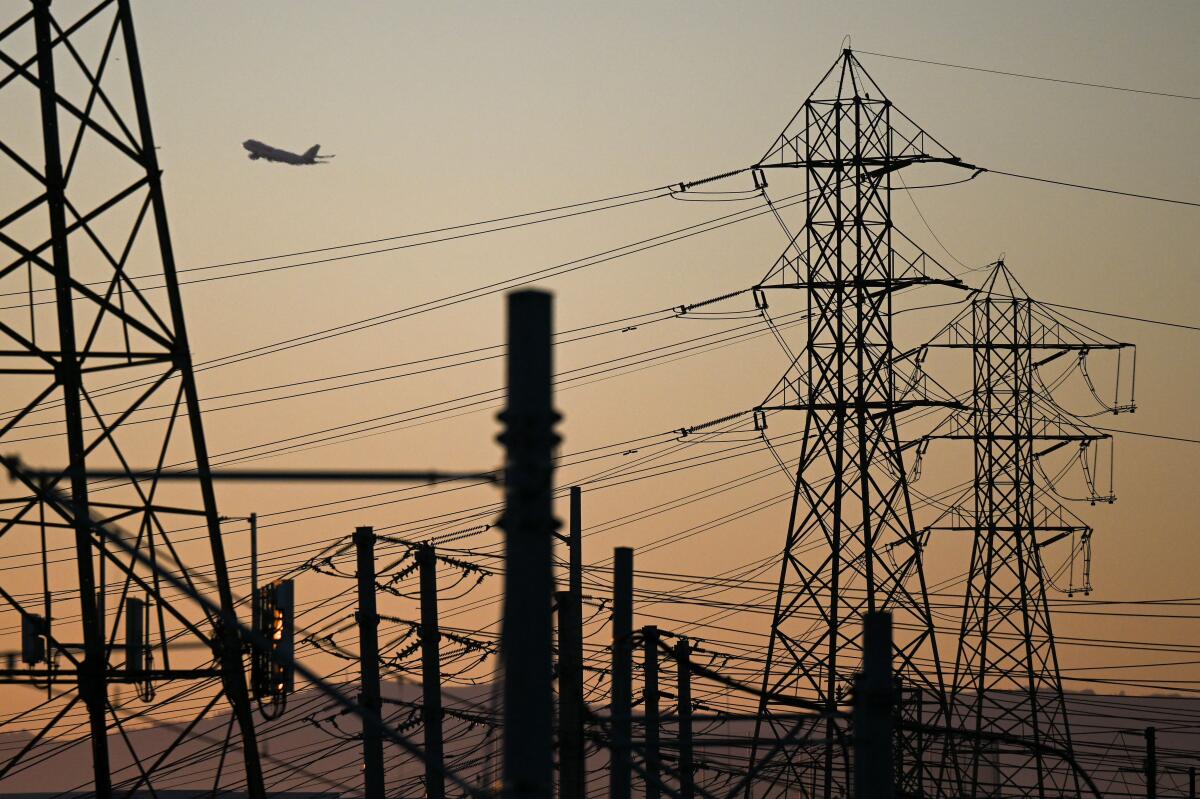 An aircraft takes off from Los Angeles International Airport (LAX) behind electric power lines at sunset 