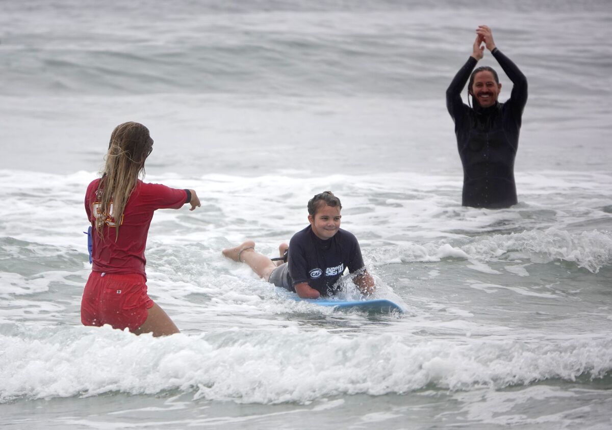 Sophia Saunders, 10, rides a wave as para surfer Liv Stone and Switchfoot drummer Chad Butler cheer her on.