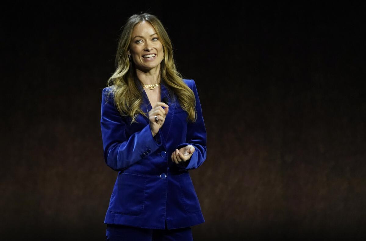 A woman speaking and wearing a dark blue velvet suit