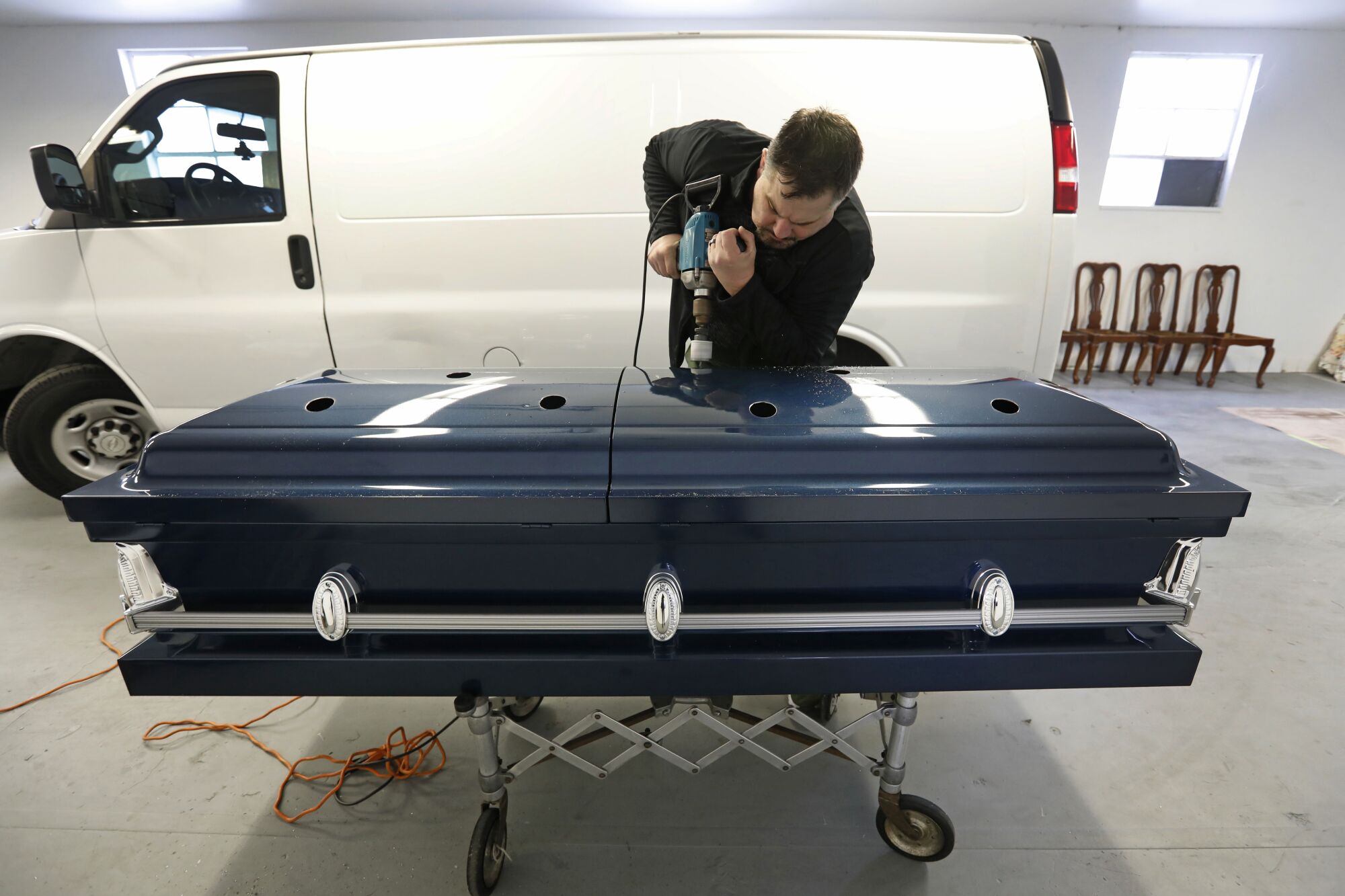 Funeral director Ken McKenzie prepares a casket by drilling holes in the aluminum and removing the inside dressings.