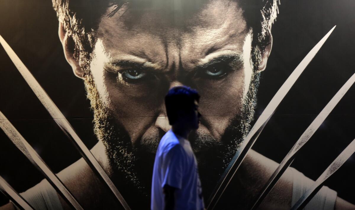 A man walks past a poster showing a scowling superhero with long metal claws