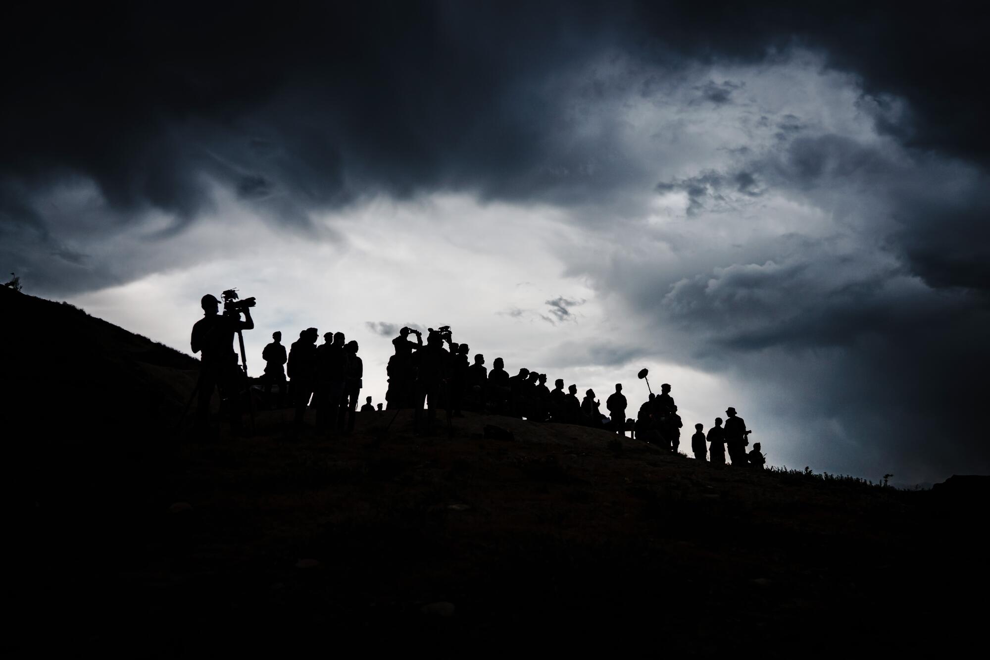 Troops and journalists are silhouetted on a hilltop