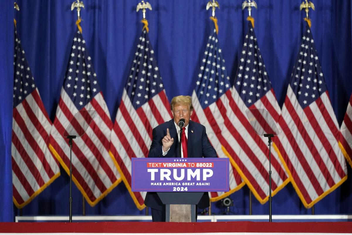 Donald Trump speaks in front of a row of American flags.