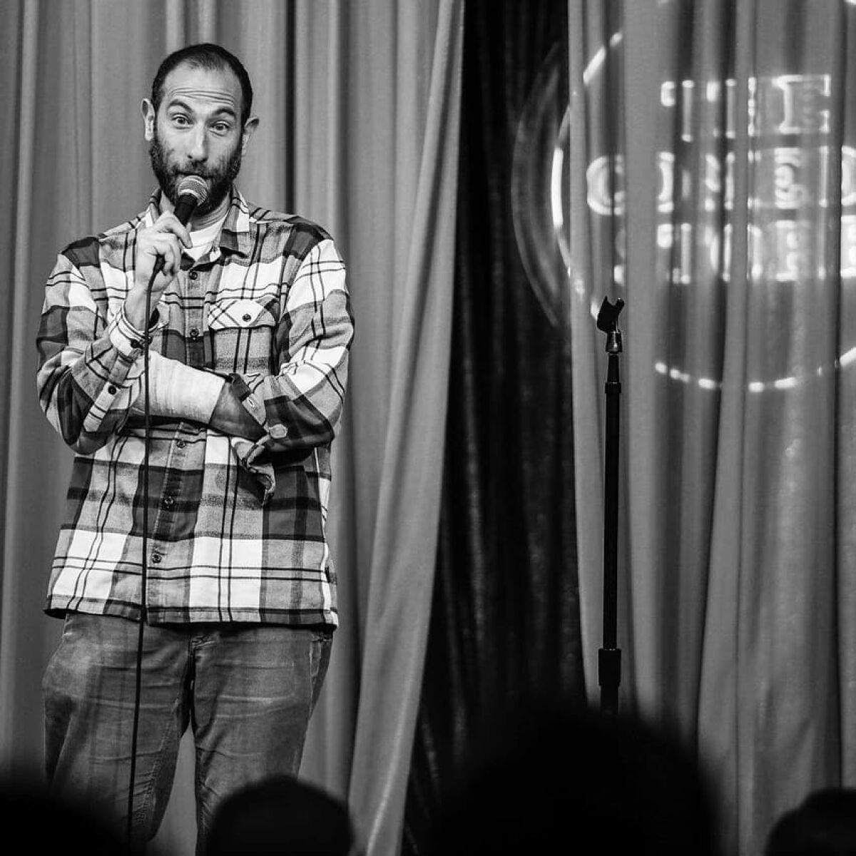 A black and white photo of a man in a flannel doing stand-up