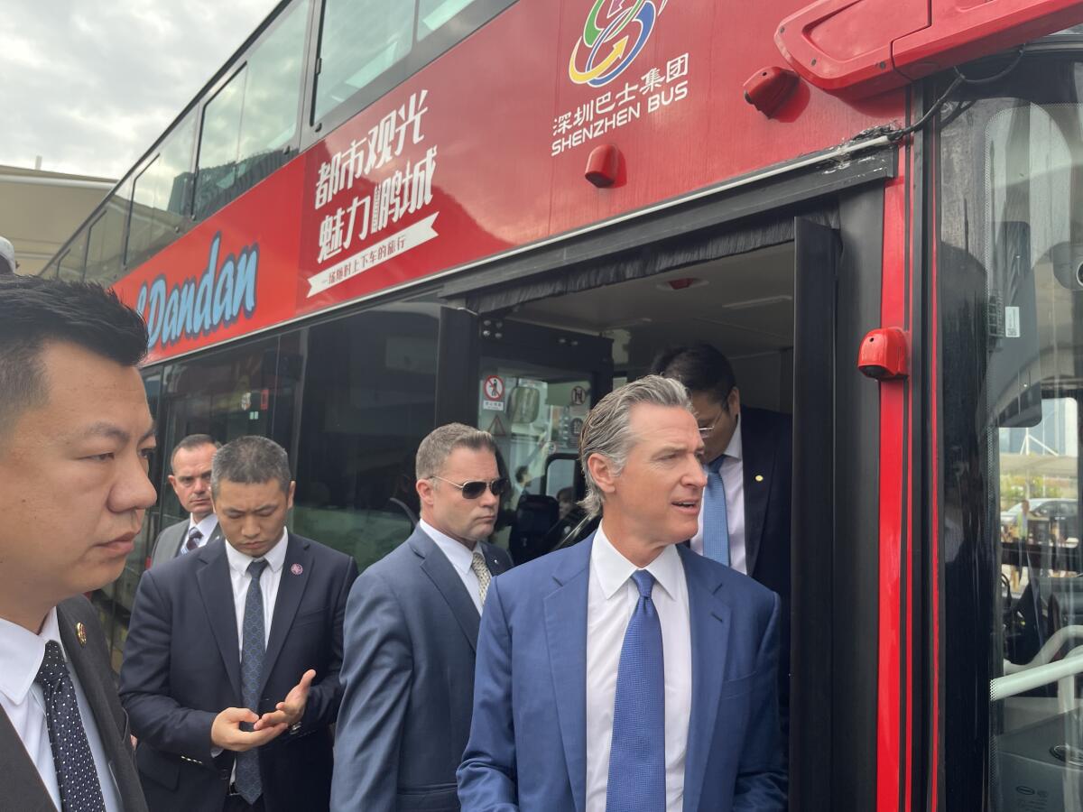 Men, including California Gov. Gavin Newsom, in front of a red electric bus