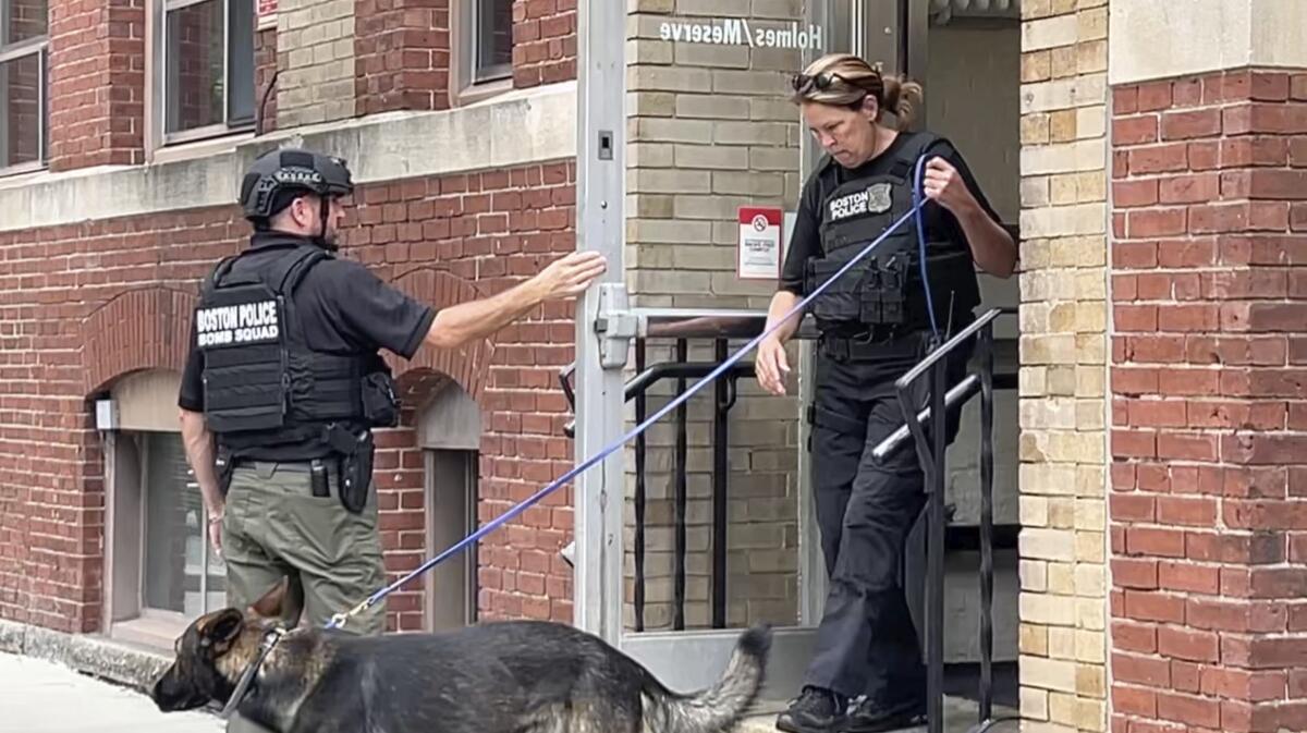 In a still photograph taken from video, a Boston Police bomb squad officer, left, and a K-9 unit officer, right, depart a building on the campus of Northeastern University, Wednesday, Sept. 14, 2022, in Boston. Law enforcement officials say authorities are examining whether the employee who reported an explosion Tuesday, Sept. 13, at Northeastern University may have lied to investigators and staged the incident. (AP Photo/Rodrique Ngowi)