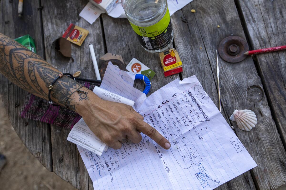 A cannabis worker points out a ledger page tallying the money owed to workers 
