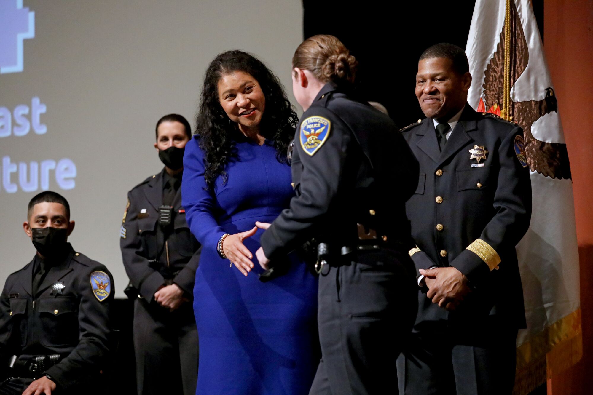 London Breed shakes the hand of a police officer while sharing the stage with three other officers