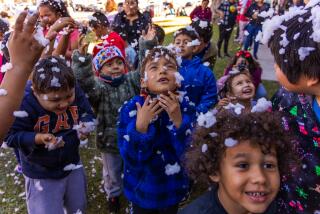 SANTA ANA, CA - DECEMBER 16: Children enjoy snow flakes falling from a snow machine while waiting in line to get toys at an annual Winter Wonderland hosted by Boys & Girls Clubs of Central Orange Coast on Saturday, Dec. 16, 2023 in Santa Ana, CA. (Irfan Khan / Los Angeles Times)