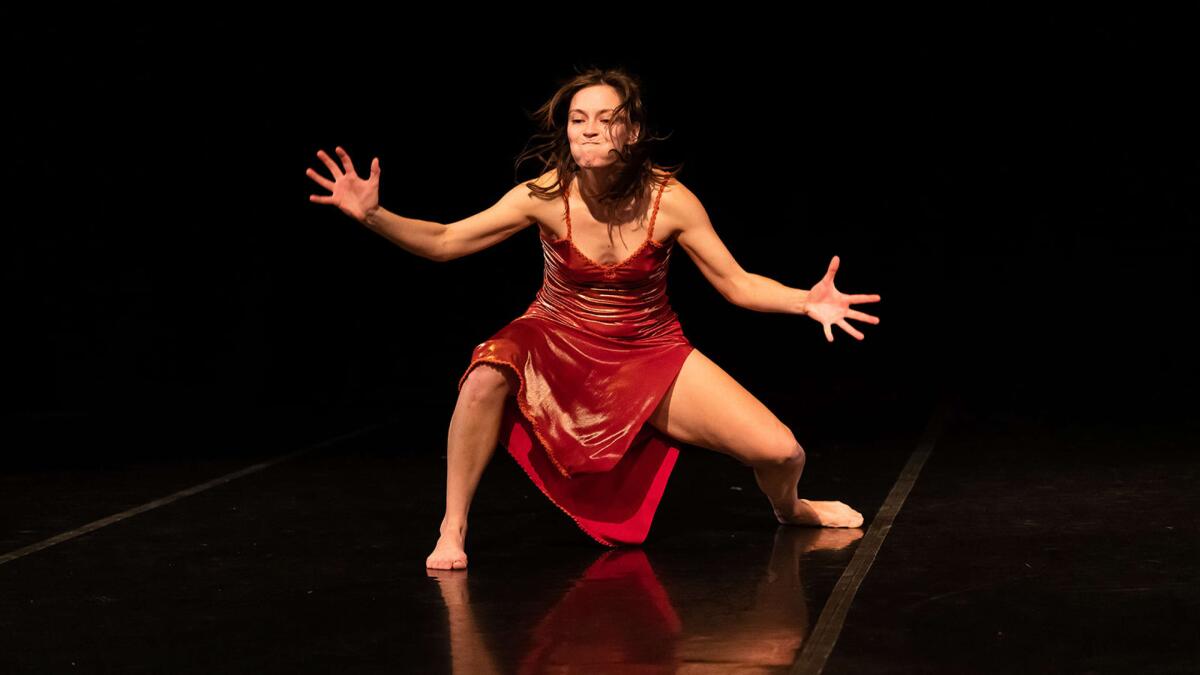 A dancer in a red dress holds her breath and extends her arms on stage.