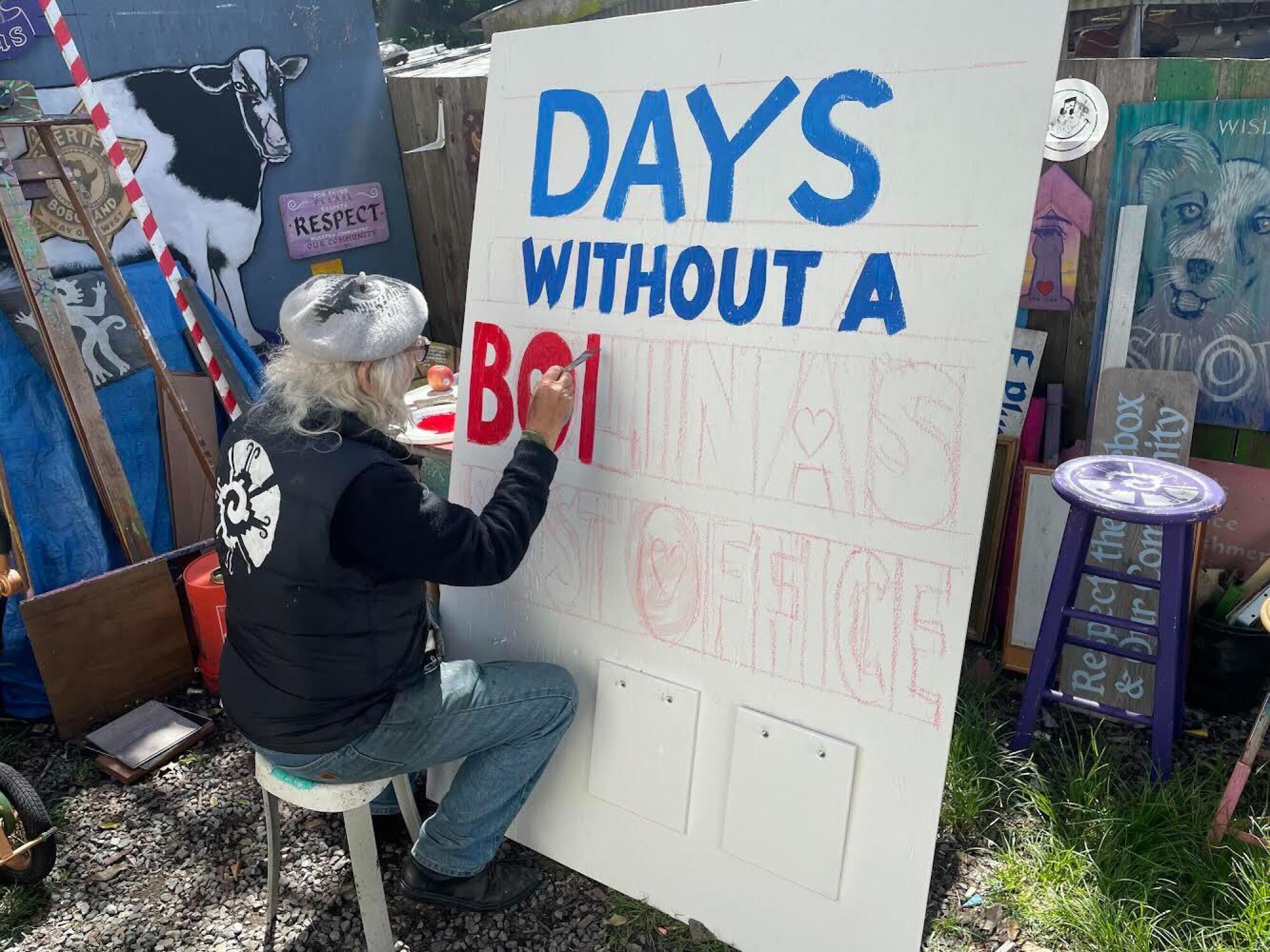 Um artista pinta uma placa branca que indica quantos dias Bolinas está sem correio.