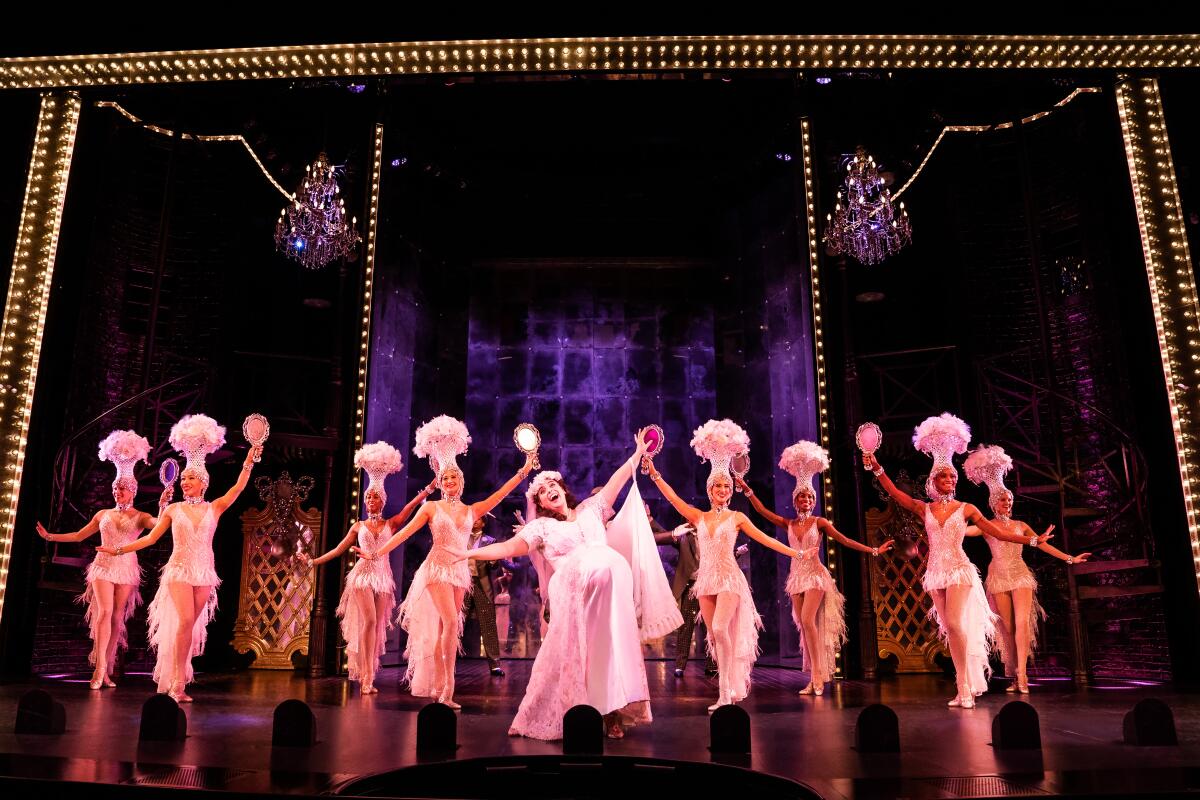 A woman in a pink dress performs in a musical backed by eight women in pink dance costumes