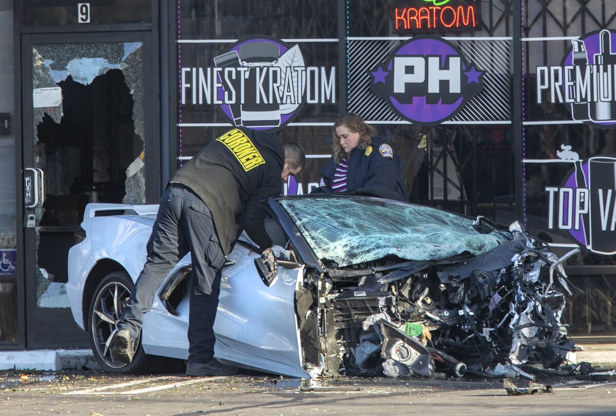 A mangled Corvette with its entire front end and engine missing lies in front of a storefront with shattered windows