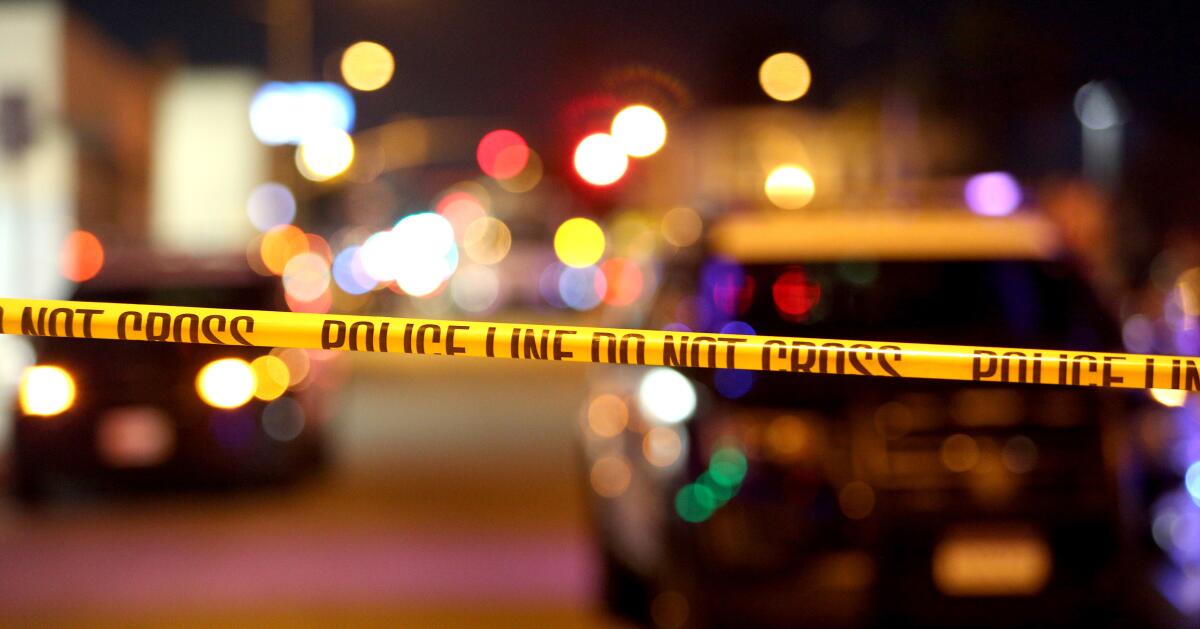 Police crime scene tape across a scene with police cars at night.