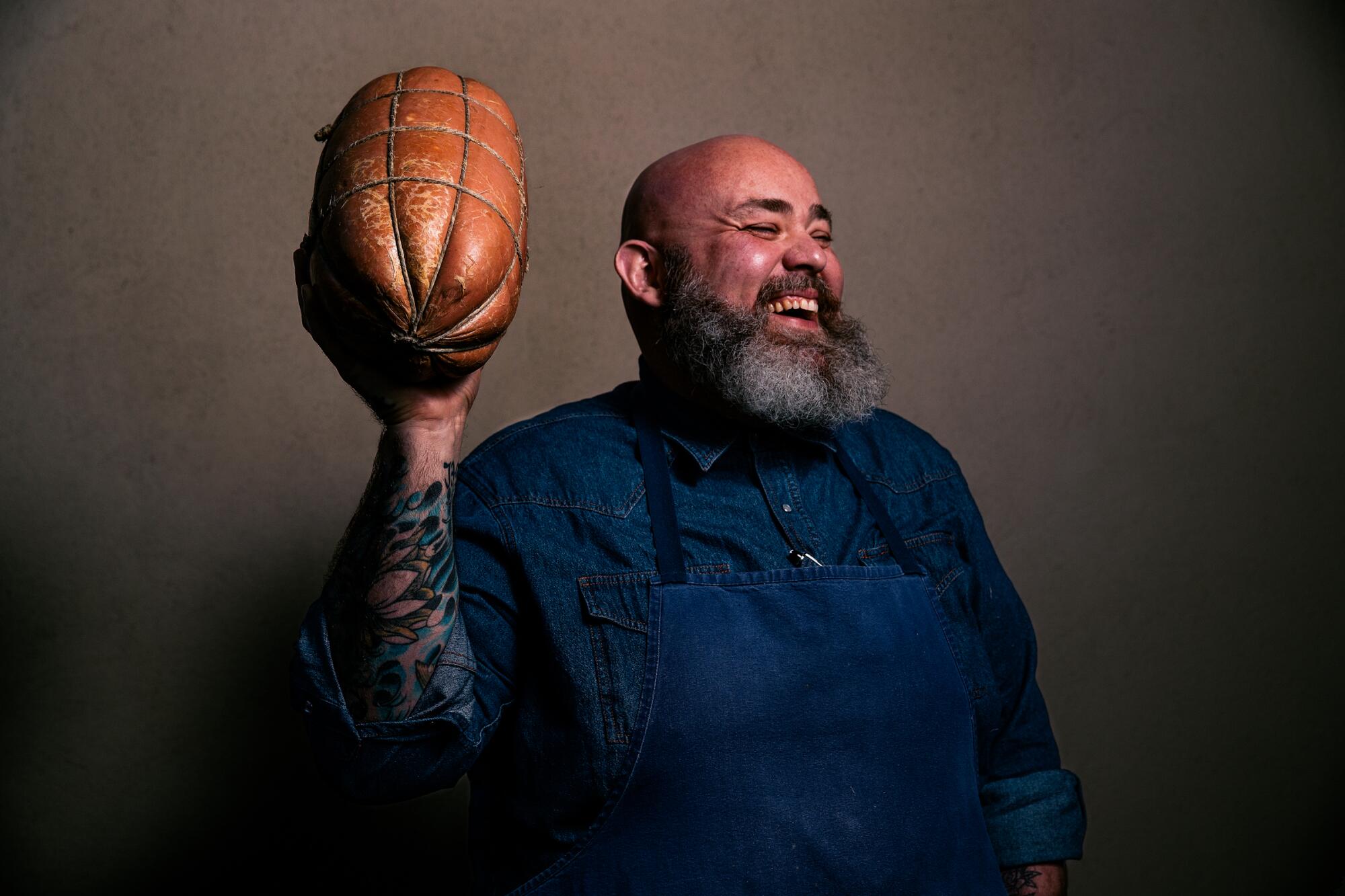 A laughing, bearded chef holds up an Italian football-shaped meat, mortadella, his favorite salumi.