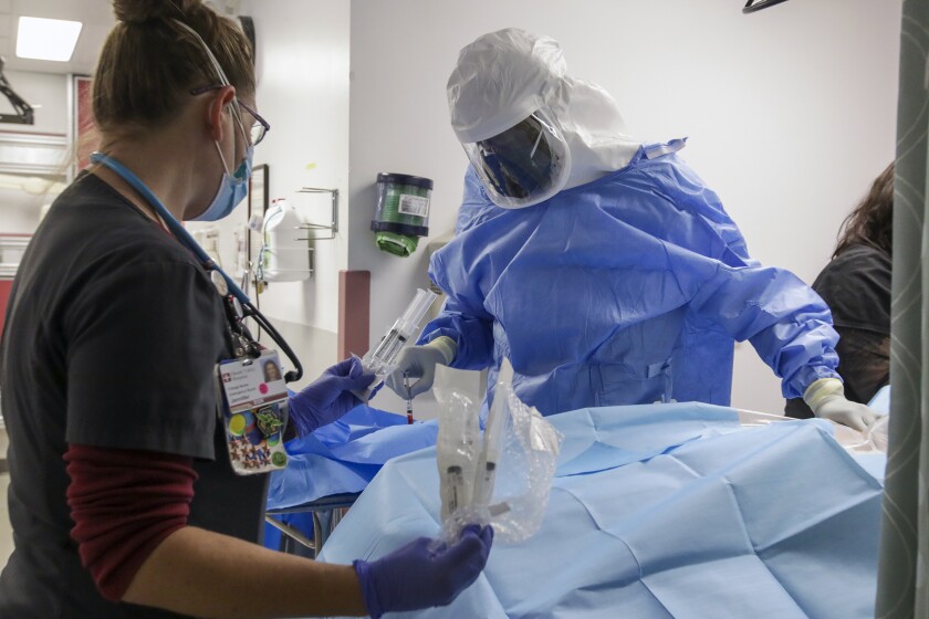 Inside an ER, a doctor and nurse in protective gear attend to a COVID-19 patient.