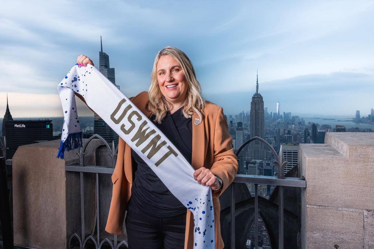 Emma Hayes holds a USWNT banner in front of the New York City skyline.