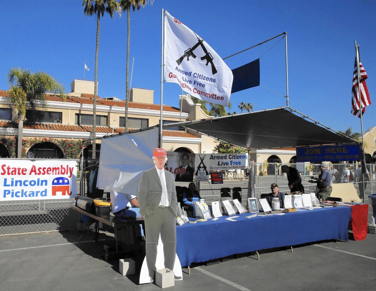 A cardboard cutout of presidential candidate Donald Trump stands at a booth where the San Diego County Armed Citizens Live Free Gun Rights Committee flag flies along with the American flag.