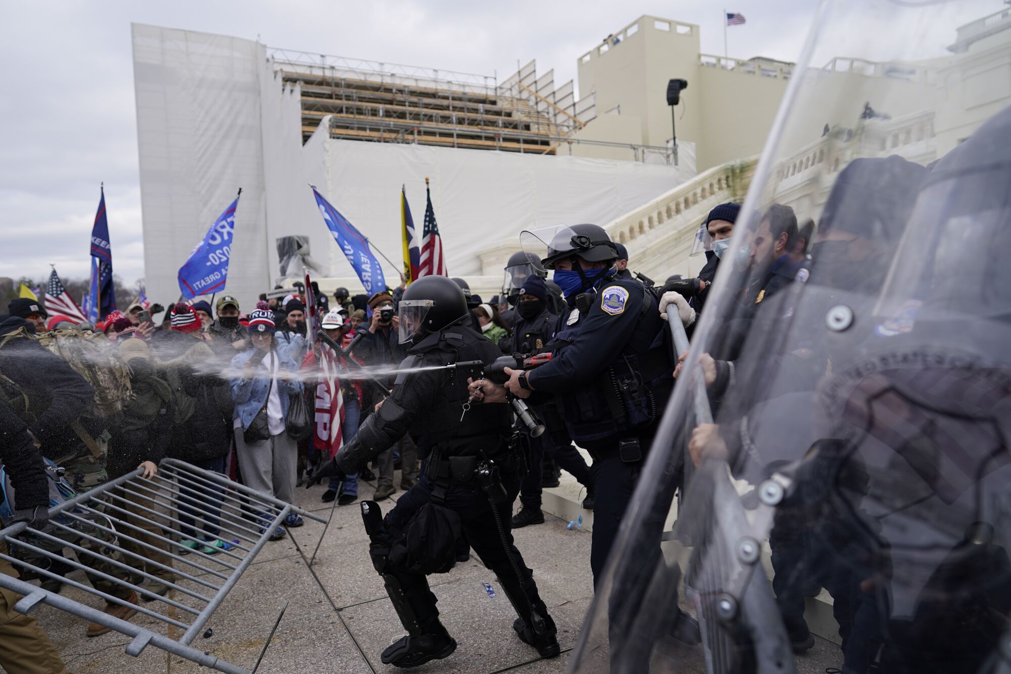 An officer shoots a stream of pepper spray at Trump supporters forcing their way through a barricade.