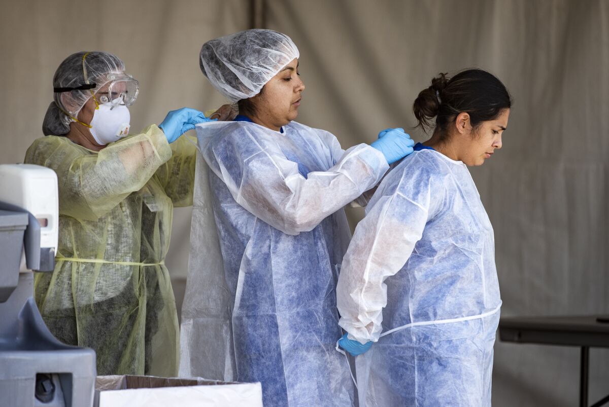 Riverside County medical personnel help one another with personal protective equipment at a drive-though coronavirus testing facility in March. A new site opened Tuesday in the county.