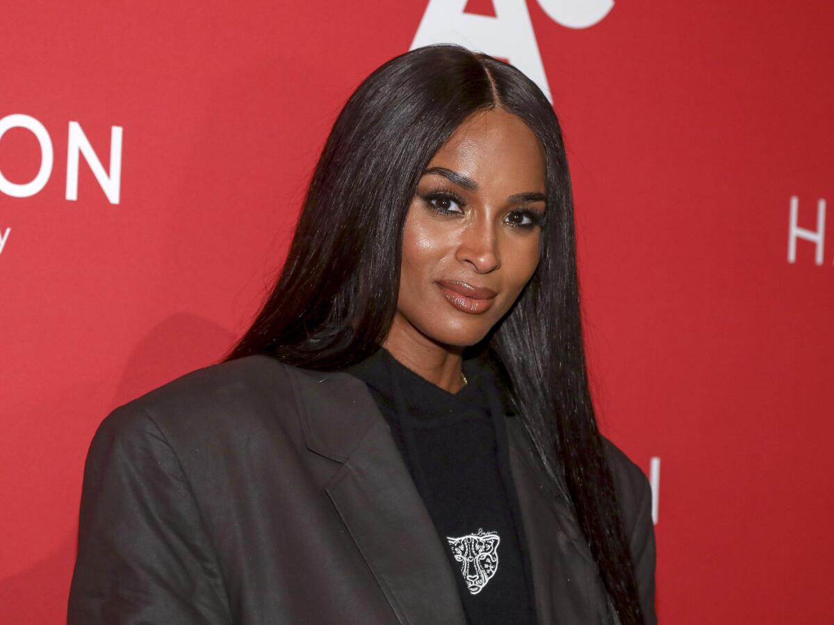 Ciara wears a dark blazer over a black shirt while posing against red backdrop
