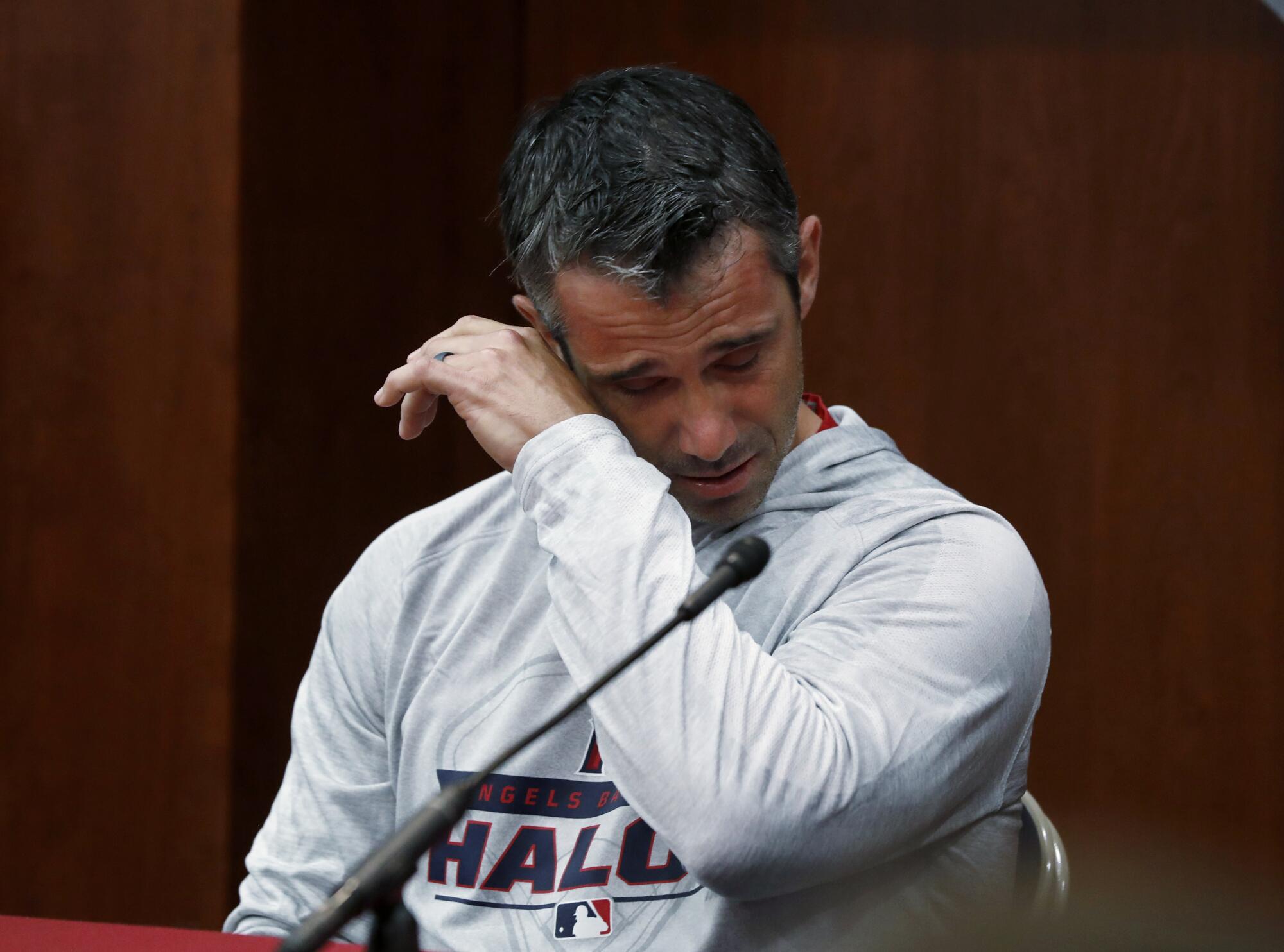 Angels manager Brad Ausmus wipes tears from his eyes while speaking near a microphone at a news conference