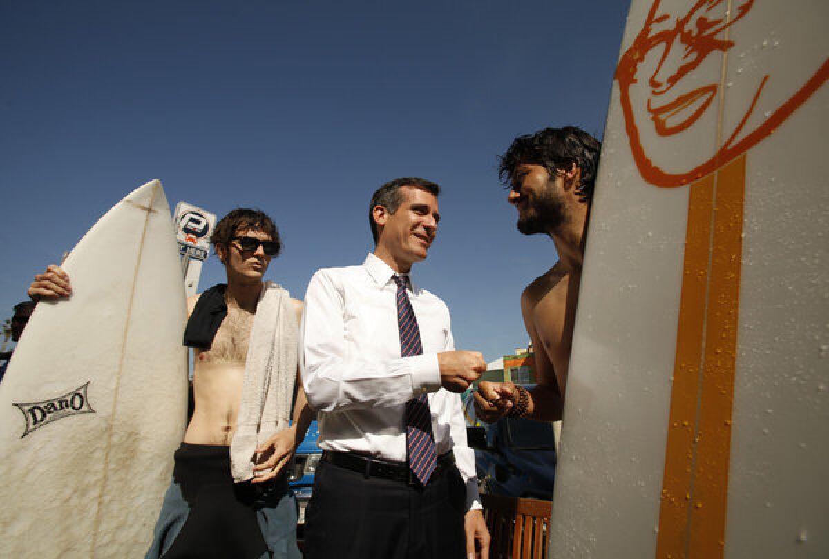 On his last day of campaigning, Los Angeles mayoral candidate Eric Garcetti gives a fist pump to surfers John D. Bondis, right, and Peyjon Olnskway, left, as he visits the Cow's End Cafe between Marina del Rey and Venice.