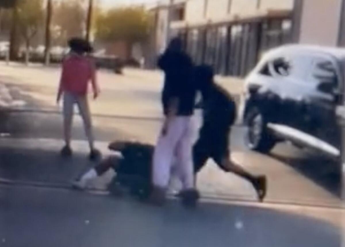 A frame from a video showing teens assaulting a man on the ground as another teen looks on