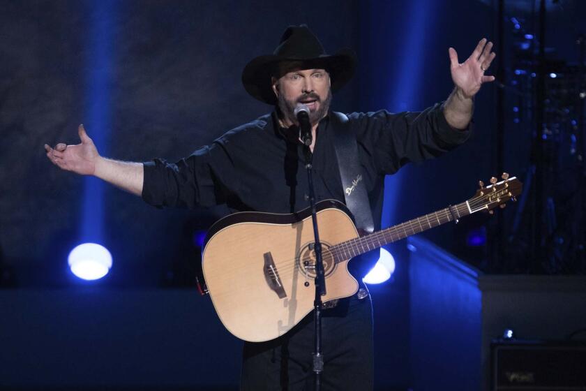 Garth Brooks holds his arms out onstage with a guitar slung around his body